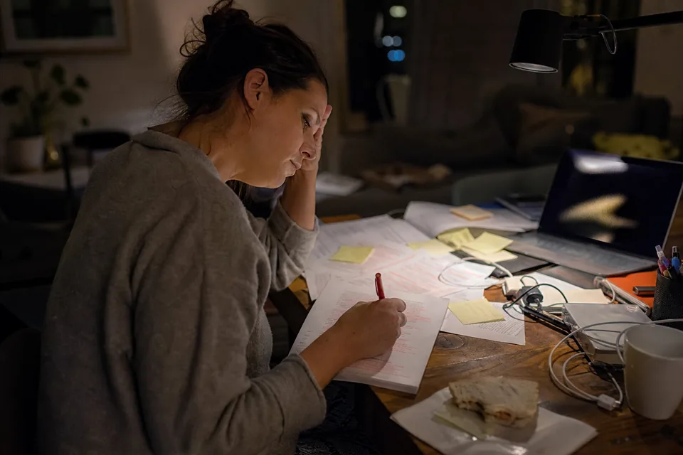 A content marketer working late at a cluttered desk, reading a printed article draft covered in pen edits next to a laptop